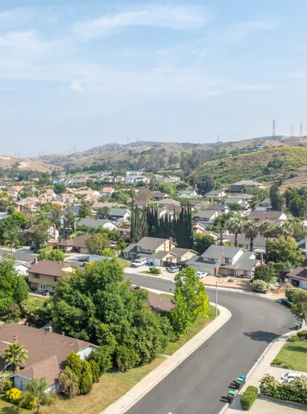 Aerial view of a Loma Linda hillside neighborhood where manicured green lawns and residential gardens back directly onto a dry, open natural slope, the kind of terrain gophers move down from into irrigated yards.