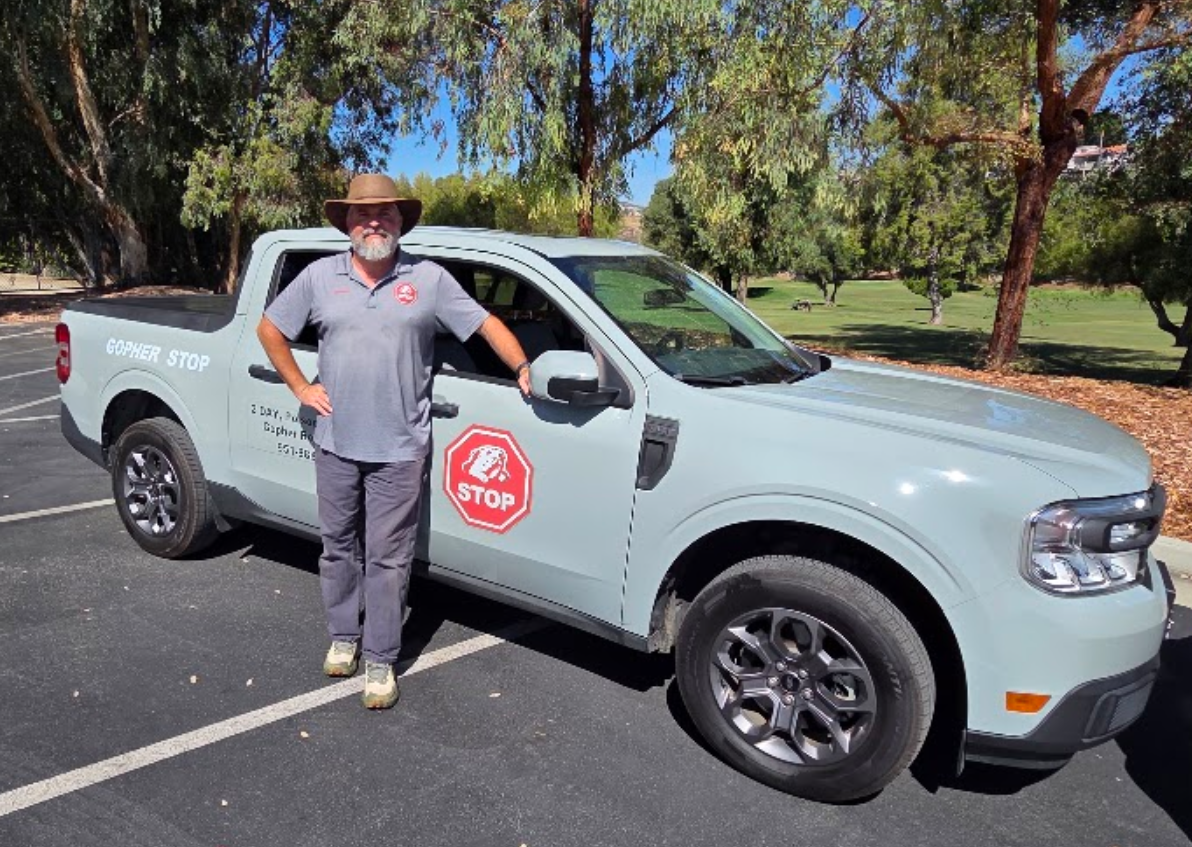 Gopher Stop technician with a branded Ford Maverick service truck parked beside a green lawn in Lake Elsinore, CA